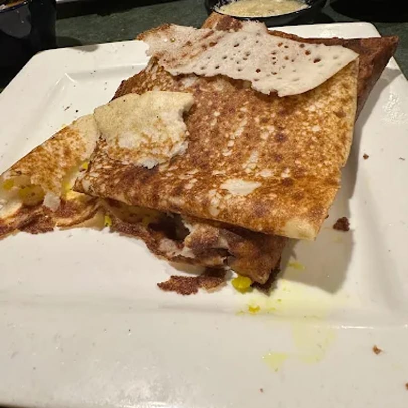 A golden-brown dosa, folded and filled with a yellow potato mixture, on a white rectangular plate.