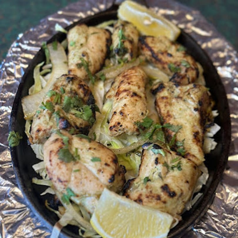 Sizzling Indian chicken tikka with onions, cilantro, and lemon wedges on a hot plate.