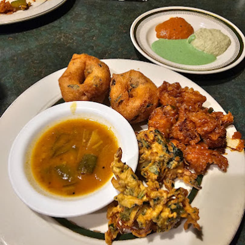 A plate of Indian appetizers including vada, pakora, and a bowl of sambar, with chutneys.