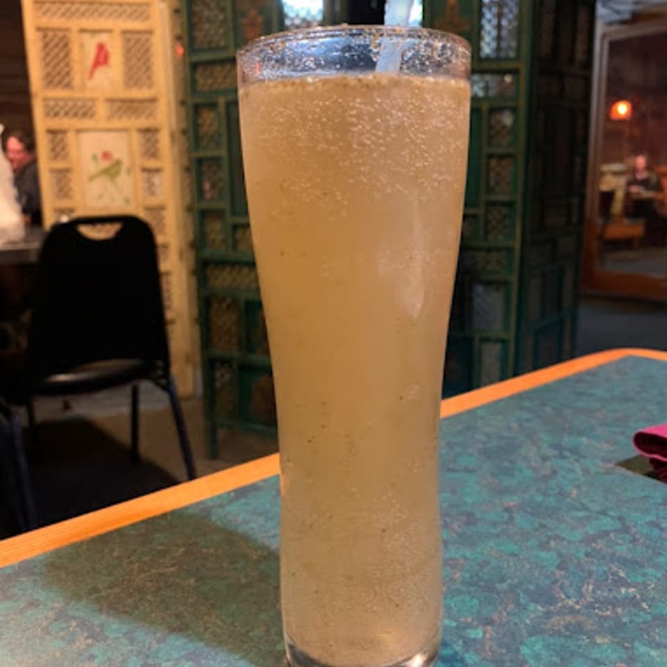 A tall glass of a light-colored, bubbly drink with a straw on a blue and orange table.