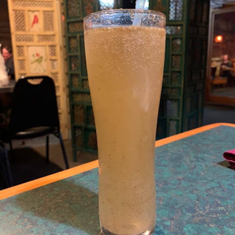 A tall glass of a light-colored, bubbly drink with a straw on a blue and orange table.