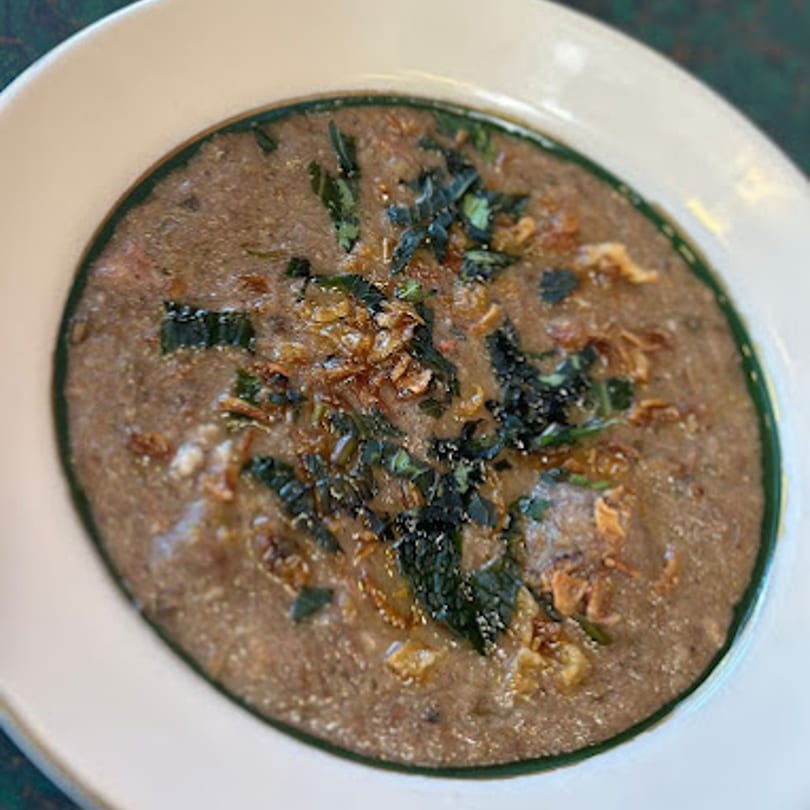 A bowl of Dakshin's Indian lentil stew, garnished with crispy fried onions and fresh herbs.