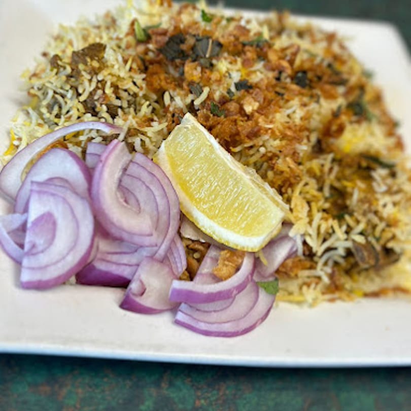 Dakshin's Indian biryani with rice, meat, fried onions, and a lemon wedge on a white plate.